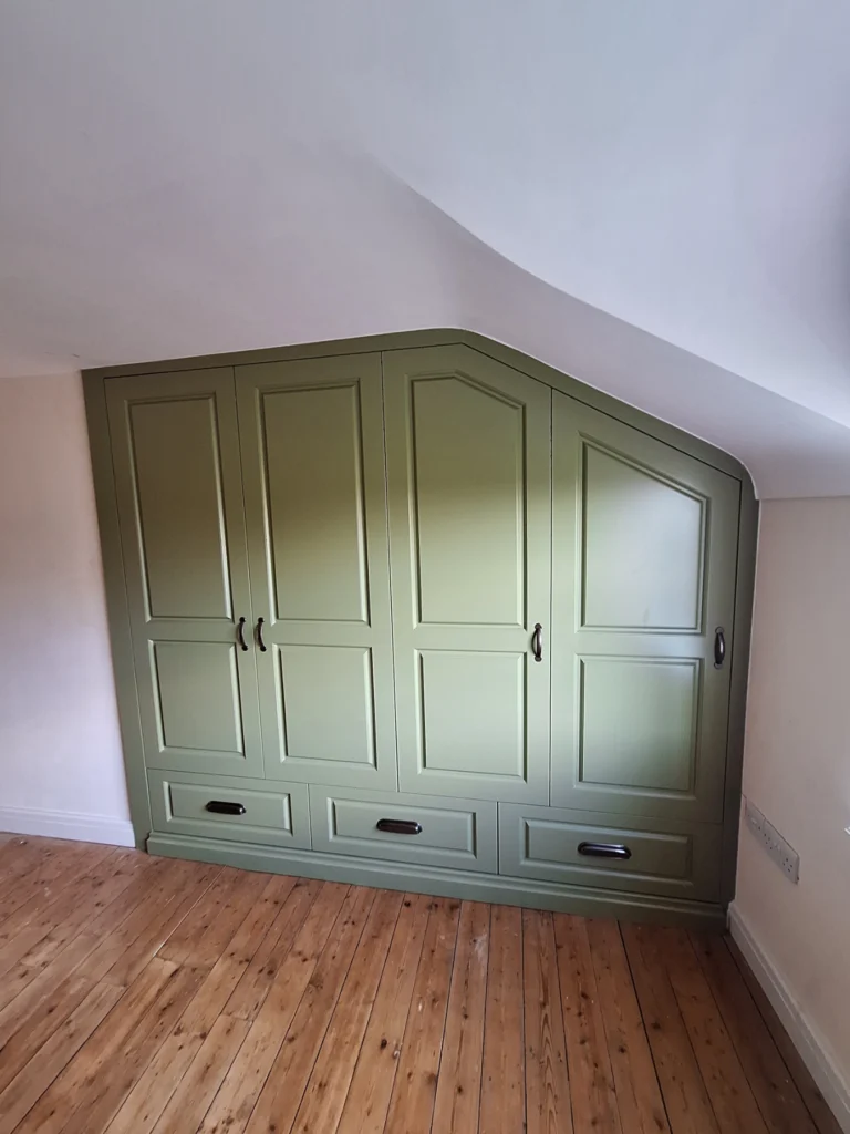 Wardrobe fitted into angled space with external drawers and raised shaker panel doors
